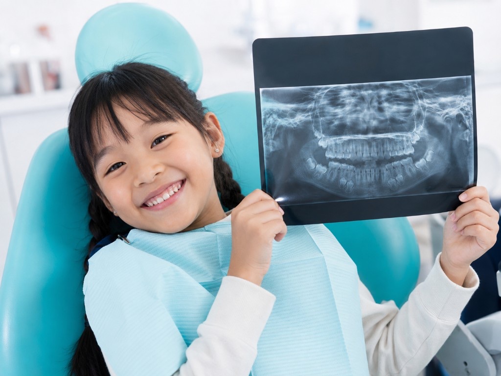 Smiling girl in the dental chair holding up a panoramic dental X-ray