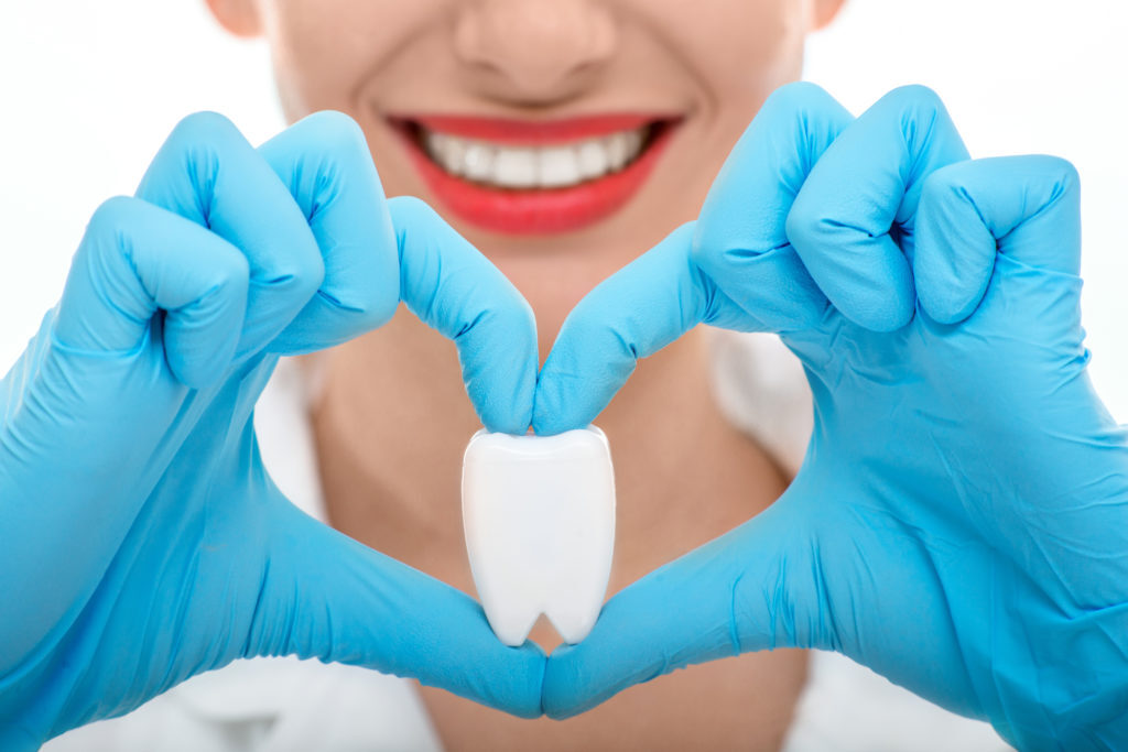 Gloved hands forming a heart shape around a model tooth in front of a smile