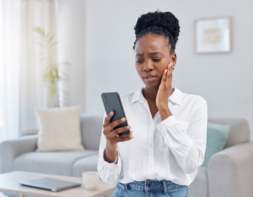 Woman holding her cheek while calling the dentist on her phone
