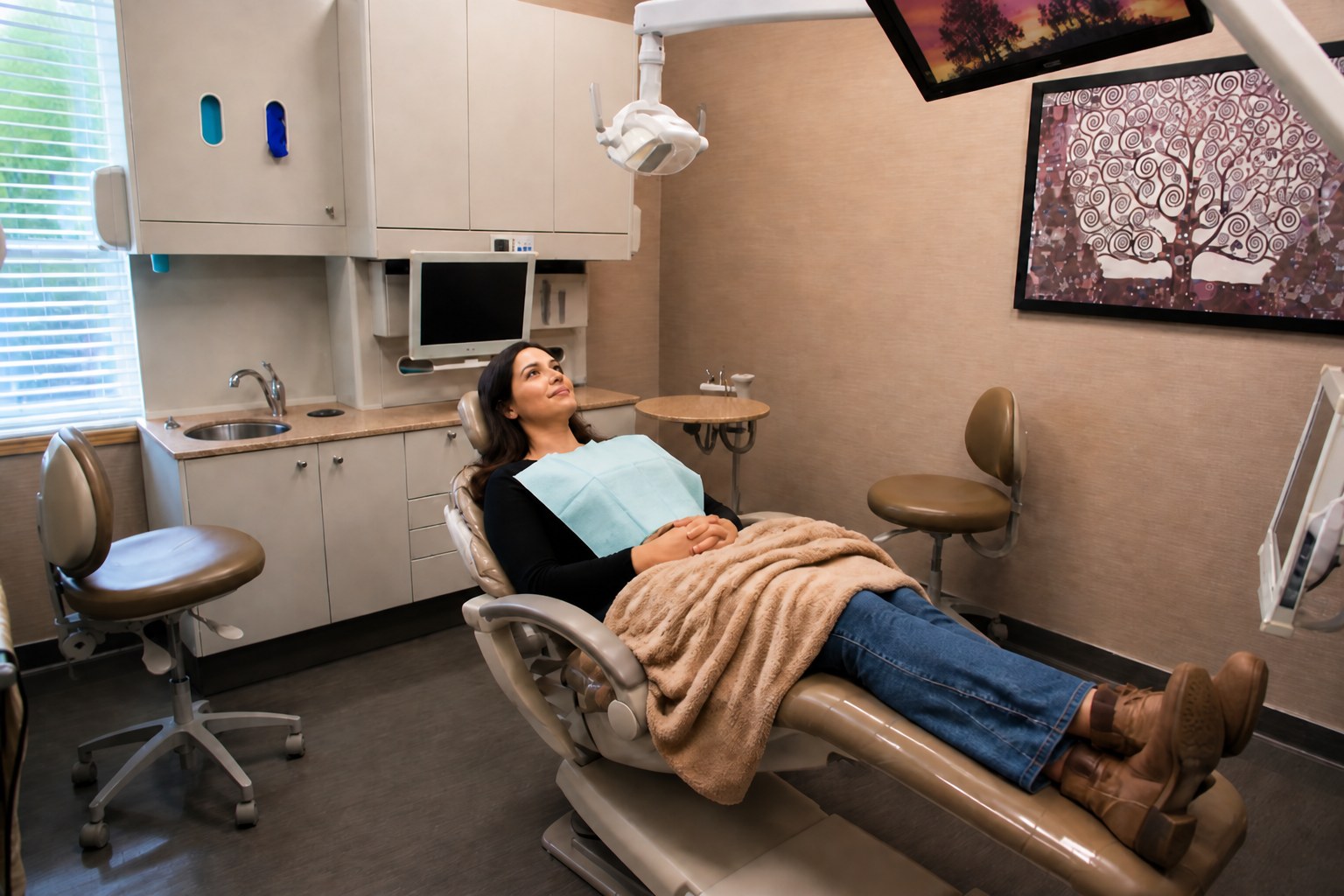 A patient relaxing under a blanket in a dental chair in a calm treatment room